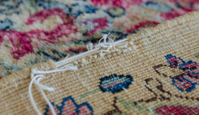 A close-up photo of a damaged rug with frayed edges and loose threads